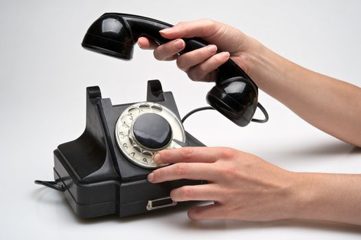 woman hand hanging up the handset of an old black telephone isolated ocer white background