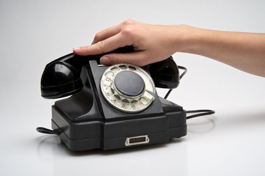 woman hand hanging up the handset of an old black telephone isolated ocer white background