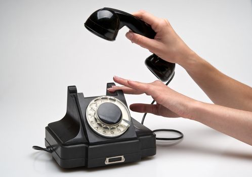 woman hand hanging up the handset of an old black telephone isolated ocer white background