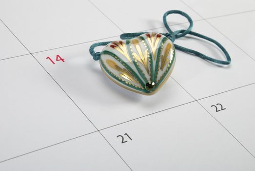 Ceramic heart-shaped pendant lying on calendar page points St. Valentine's day