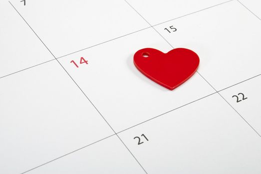Red heart sign laying on calendar page points St. Valentine's day