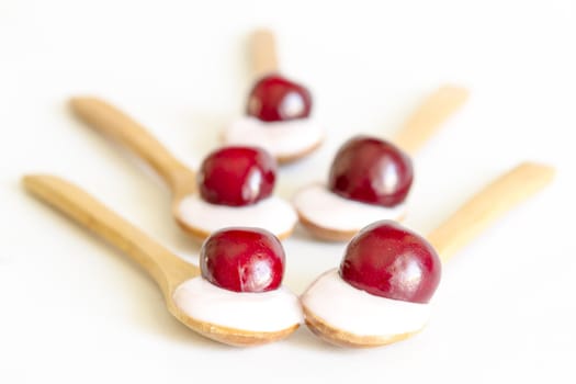 Wooden spoon is with yogurt and fresh cherries on white background