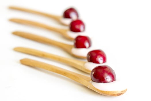 Wooden spoon is with yogurt and fresh cherries on white background