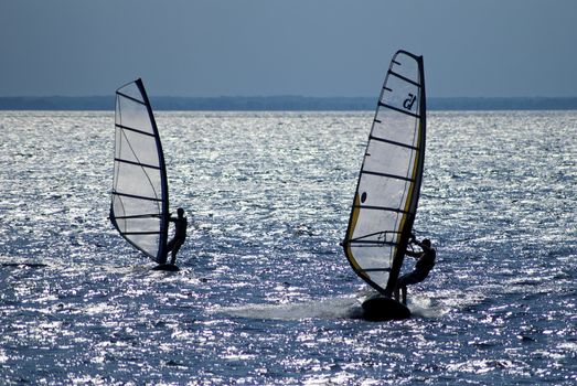 Two windsurfers in patches of light of a sunlight