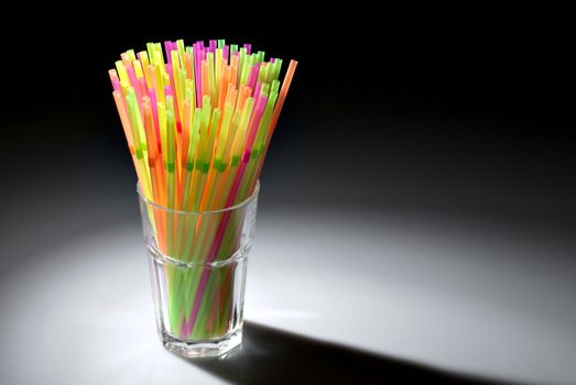 Multicolor flexible straws in the glass in spot of light isolated on black background
