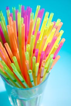 Multicolor flexible straws in the glass on blue background. Macro with small depth of field