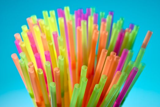 Multicolor flexible straws in the glass on blue background. Macro with small depth of field