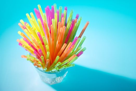 Multicolor flexible straws in the glass on blue background. Macro with small depth of field