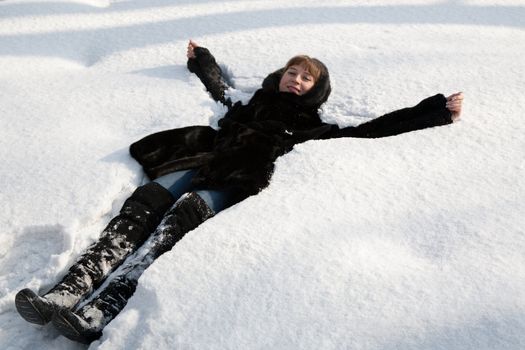 The young girl in a black fur coat lays in a snow