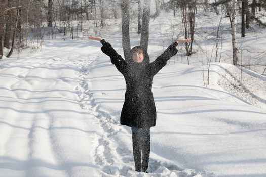 The young girl in a black fur coat stands under a snow strewed on her