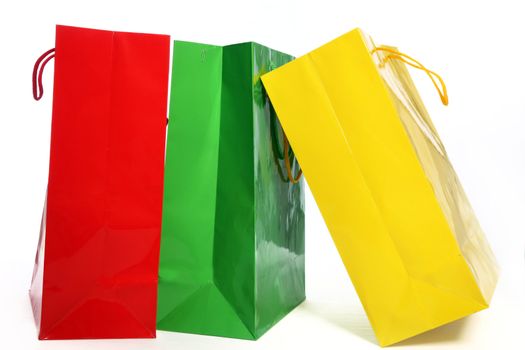 Three colourful paper shopping bags in red, green and yellow suitable for recycling standing on a white background