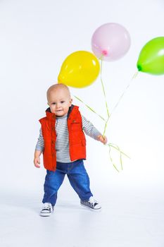 Cute funny little boy in a red vest with colored balloons. In the studio