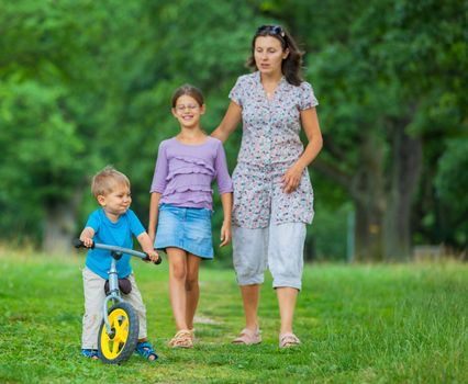 Portrait of little boy on a bicycle and his mother and sister in the summer park