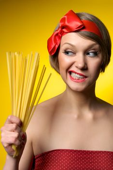 Portrait of young housewife holding pasta in her hand. Retro styled. Isolated on yellow background