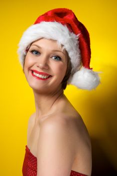 Pretty christmas girl wearing red dress and santa hat, smiling. Isolated on yellow background