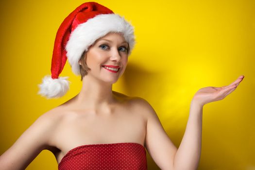 Pretty christmas girl wearing red dress and santa hat, smiling. Isolated on yellow background