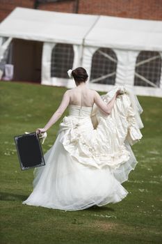 Pretty bride in wedding dress walking away from camera holding a blank board with space for copy