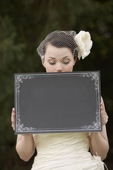 Pretty bride in wedding dress holding a blank board in front of face with space for copy