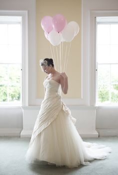 pretty bride in her wedding dress holding ballons in front of windows