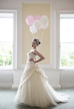 pretty bride in her wedding dress holding ballons in front of windows