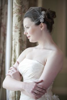 Pretty bride looking out of window and smiling on her wedding day