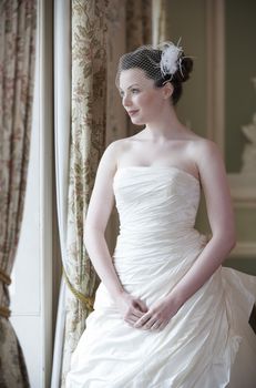 Pretty bride looking out of window and smiling on her wedding day