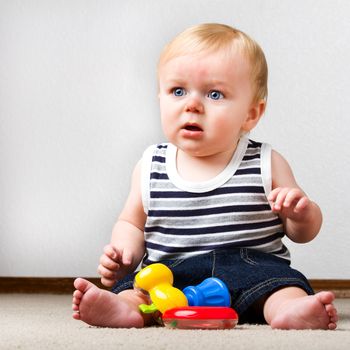 Young toddler sitting up on the floor with a ring and a toy hammer to play with.