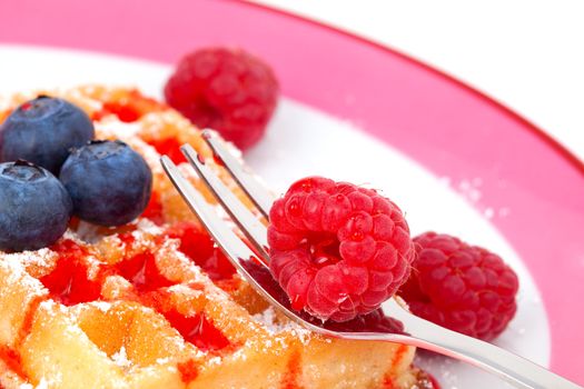 belgian waffles with syrup or  served on a plate, garnished with raspberries and blueberry