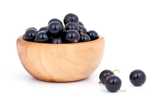 fresh black currants in a wooden bowl, over a white background.