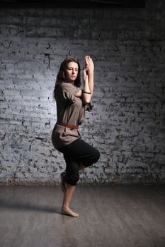 Full-length portrait of young beautiful woman doing yoga excercise against a brick wall