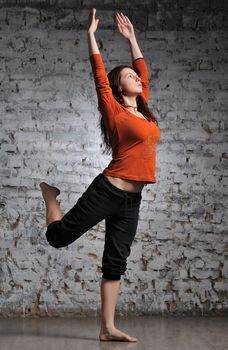 Full-length portrait of young beautiful woman doing yoga excercise against a brick wall