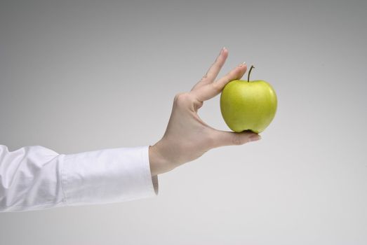 Woman's hand holding green apple over light background