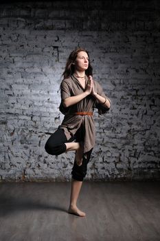 Full-length portrait of young beautiful woman doing yoga excercise against a brick wall