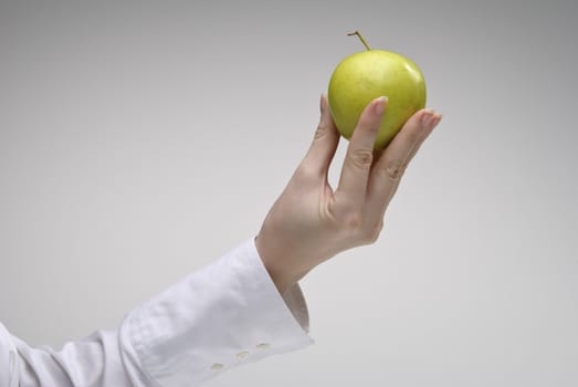 Woman's hand holding green apple over light background