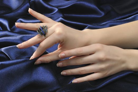 Close-up woman's hands with ring on sliky blue background