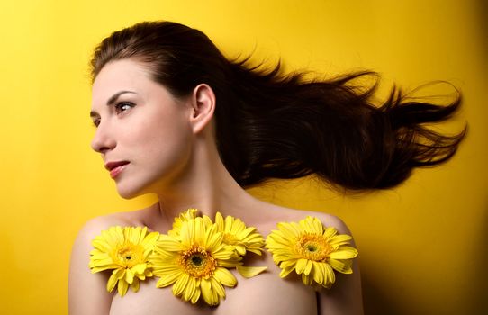 Topless portrait of a beautiful young woman covered with yellow flowers isolated on yellow background