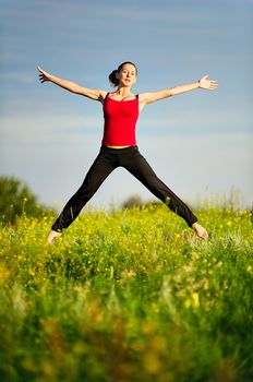 Happy young woman in sport wear jumping on a sunset field