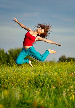 Happy young woman in sport wear jumping on a sunset field