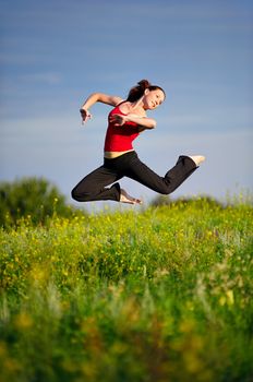 Happy young woman in sport wear jumping on a sunset field