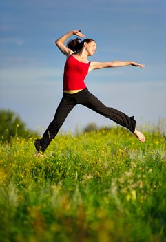 Happy young woman in sport wear jumping on a sunset field