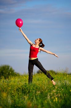 Happy young woman in sport wear jumping with red balloon on a sunset field