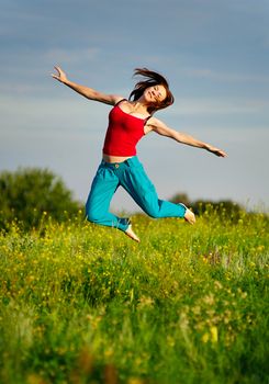 Happy young woman in sport wear jumping on a sunset field