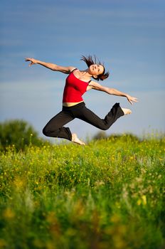 Happy young woman in sport wear jumping on a sunset field