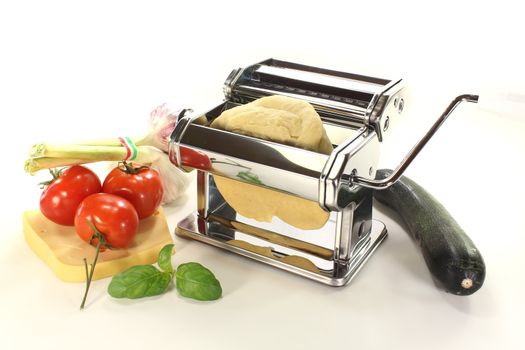 Noodle dough in a pasta machine with tomatoes, chili and basil