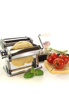 Noodle dough in a pasta machine with tomatoes, cheese and basil