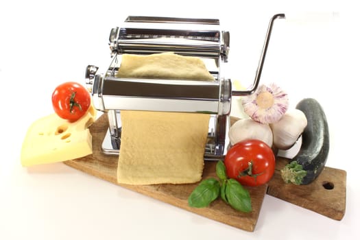 Noodle dough in a pasta machine with vegetables, cheese and basil