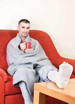 man with a broken leg on a sofa at home  holding cp of coffee