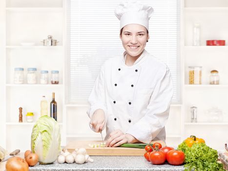 Young female chef cutting onions on the cutting board in kitchen