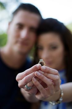 Young happy couple holding a diamond engagement ring.  Shallow depth of field with sharp focus on the ring.