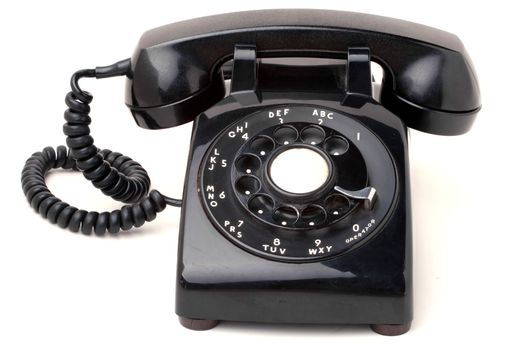 An old black antique rotary style telephone isolated over a white background.